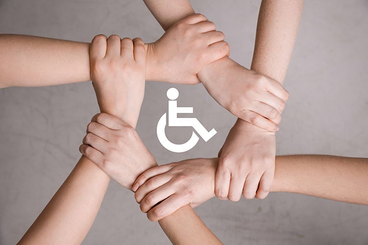 Inclusion concept. People holding hands together around international symbol of access together on grey background, top view/ shutterstock.com