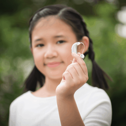 Out-of-focus image of an asian girl holding up a hearing aid